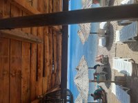 Blick von der überdachten Sitzfläche auf Liegen, Strohschirme und das Meer